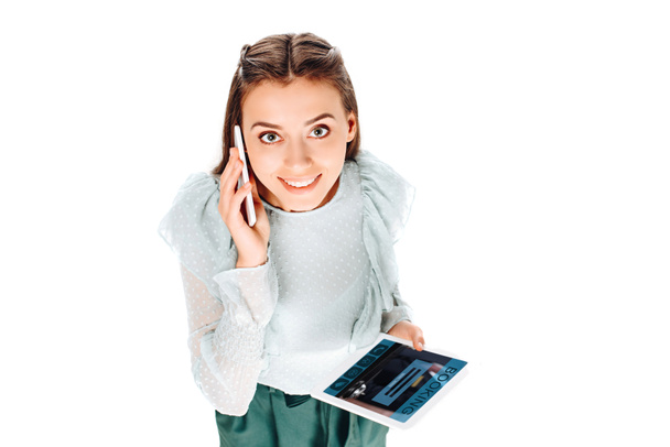Hochwinkel-Ansicht einer lächelnden Frau mit Tablet im Gespräch auf Smartphone isoliert auf Weiß - Foto, Bild