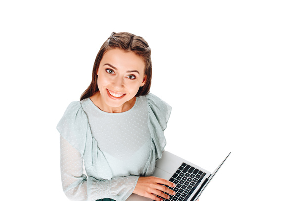 genç gülümseyen kadın üzerinde beyaz izole dizüstü bilgisayar ile yüksek açılı görünüş - Fotoğraf, Görsel