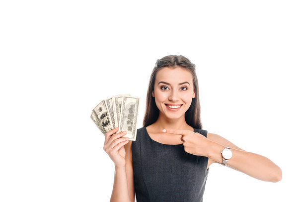 smiling woman in black dress pointing at dollar banknotes isolated on white - Foto, immagini