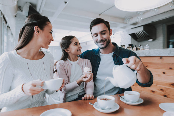 Family Resting in Cafe. Family is a Mother, Father, Daughter and Son. People is Eating Cakes and Drinking a Tea. Persons is Sitting at Table. People is Happy and Smiling. Sunny Daytime. - Foto, Imagen