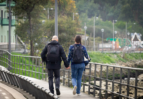 Łysy mężczyzna i kobieta z kucyk spacerem wzdłuż promenady, w pobliżu rzeki, z rąk organizowane wspólnie. Widok z tyłu. - Zdjęcie, obraz
