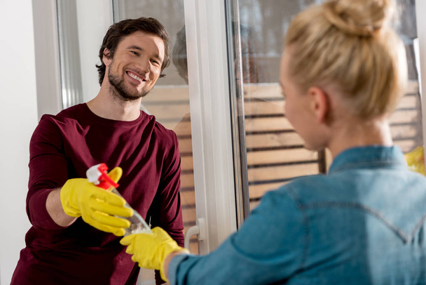 girl in rubber gloves giving cleaning spray to smiling husband - Photo, image