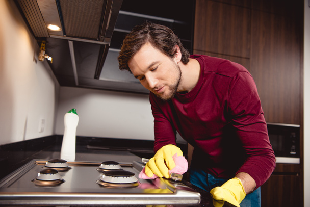 handsome man in rubber gloves cleaning kitchen - Фото, изображение