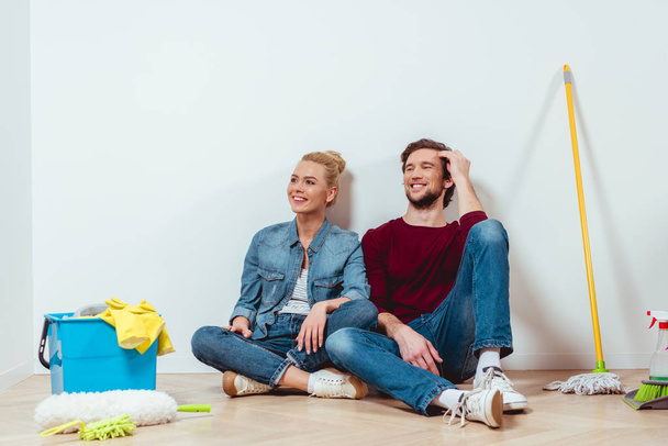 счастливая семейная пара, сидящая на полу рядом с уборочным оборудованием в квартире
 - Фото, изображение