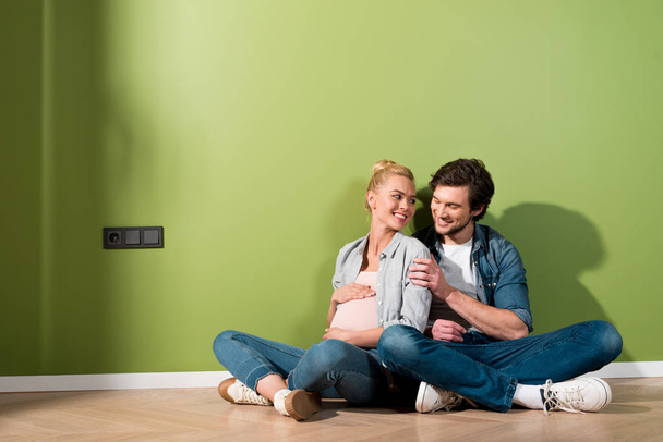 smiling man sitting on floor and embracing pregnant wife - Fotoğraf, Görsel