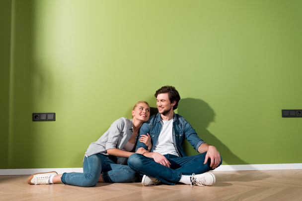 loving couple sitting on floor and looking at each other by green wall - Foto, Bild