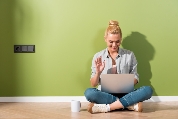 beautiful girl smiling, sitting on floor by green wall and using laptop - 写真・画像