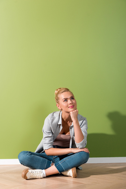 pensive girl sitting on floor by green wall - Photo, image