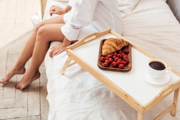 обрезанный снимок женщины, сидящей на кровати с завтраком на подносе дома
 - Фото, изображение