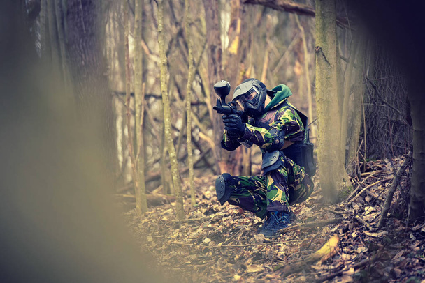 Paintball player in protective uniform and mask aiming gun in the forrest cover - Фото, изображение