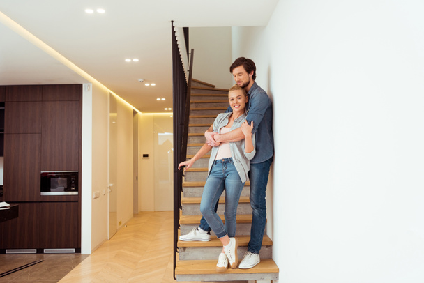handsome man embracing beautiful wife on stairs at home - Φωτογραφία, εικόνα