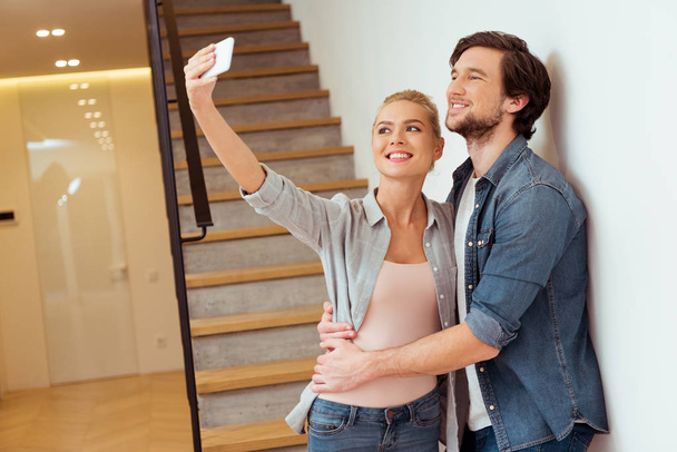 alegre familia pareja tomando selfie cerca escaleras en casa
 - Foto, Imagen