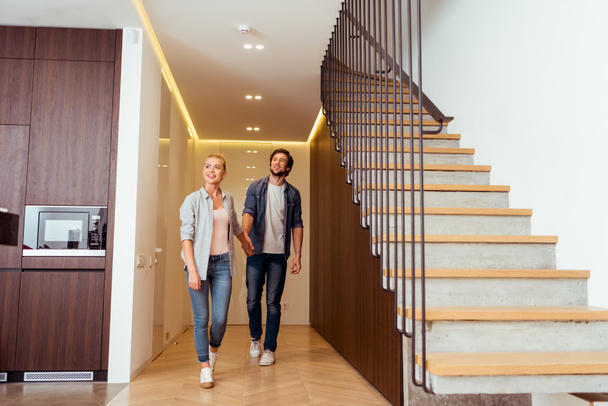 cheerful couple holding hands near stairs at home - Photo, Image