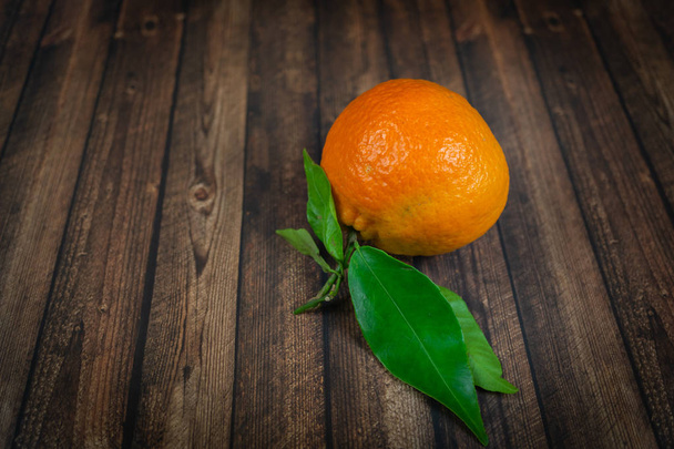 Mandarina con hojas verdes sobre fondo de madera
 - Foto, imagen