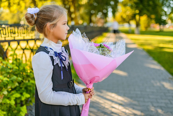 Hermosa niña con gran ramo de flores en el día del conocimiento (comienzo del año escolar) cerca de la escuela
. - Foto, Imagen