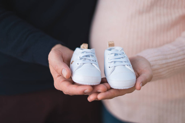 Husband and pregnant woman holding baby shoes, closeup - Фото, изображение