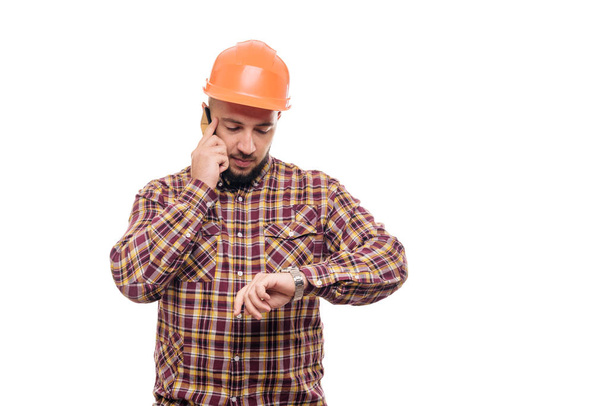 An angry and nervous worker in an orange helmet is talking loudly on the phone, shouting into the phone. Isolated white background - Foto, immagini