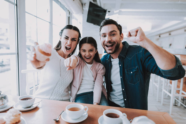 Family Resting in Cafe. Family is a Mother, Father and Daughter. Angry Moyher is Showing a Cake. Daughter is Pointing to Camera. Father and Daughter is Happy and Smiling. Persons is Sitting at Table. - Foto, imagen