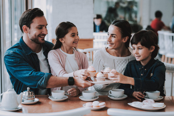 Family Resting in Cafe. Family is a Mother, Father, Daughter and Son. People is Eating Cakes and Drinking a Tea. Persons is Sitting at Table. People is Happy and Smiling. Sunny Daytime. - 写真・画像