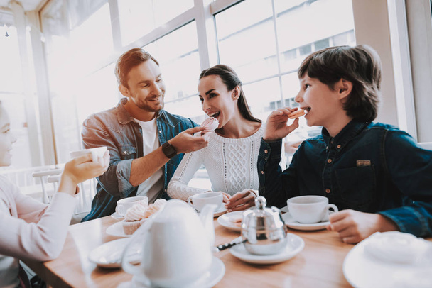 Family is Resting in Cafe. Family is a Mother, Father, Daughter and Son. People is Eating a Cakes and Drinking a Tea. Persons is Sitting at Table. People is Happy and Smiling. Daytime. - Foto, Imagen