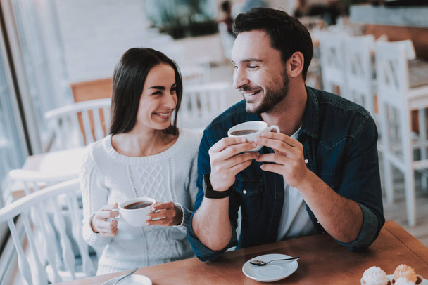 Couple Resting in Cafe. Couple is Beautiful Young Man and Woman. Couple is Drinking Tea. People is Looking on Each Other. Persons is Sitting at Table. People is Happy and Smiling. Daytime. - Foto, imagen