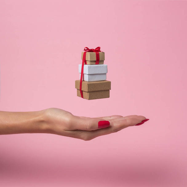 Womans hand holding gift boxes on pink background. Minimal sale concept. - 写真・画像