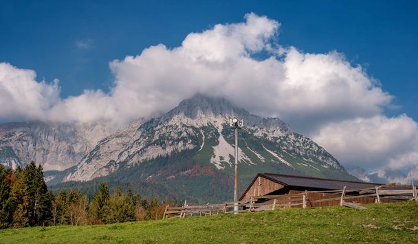 Alpine landscape on a sunny day. Colorful autumn scene. Mountain and a huge cloud above it. In the foreground is a relay tower and an alpine shed. Amazing natural background. South Tyrol Austria - 写真・画像