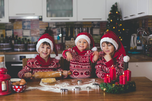 Dulce niño pequeño y su hermano mayor, niños, ayudando a mamá a preparar galletas de Navidad en casa en la cocina - Foto, imagen