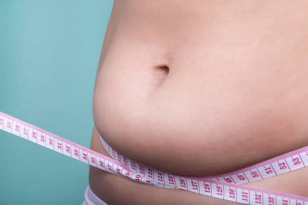 close-up female belly with overweight wrapped with a measuring tape, the concept of proper nutrition and diet for weight loss - Foto, imagen