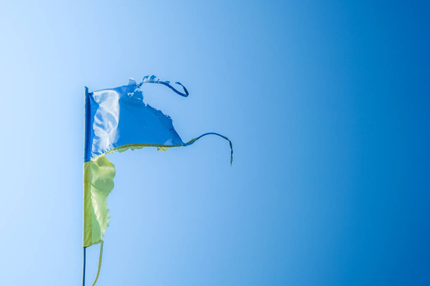 пошарпаний українським прапором майорить у вітер проти синього неба - Фото, зображення