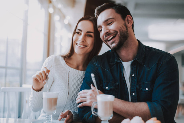Couple Resting in Cafe. Couple is Beautiful Young Man and Woman. Persons is Sitting at Table. People is Happy and Smiling. People is Drinking Latte and Eating a Cakes. Sunny Daytime. - 写真・画像