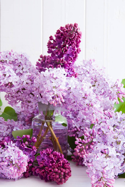 Purple flowers of lilac with leaves in a glass bottle on a white wooden background - Photo, image