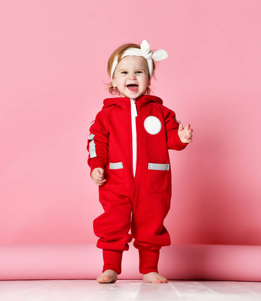 Infant child baby boy kid toddler in redbody cloth make first steps standing happy looking up on light pink  - Φωτογραφία, εικόνα