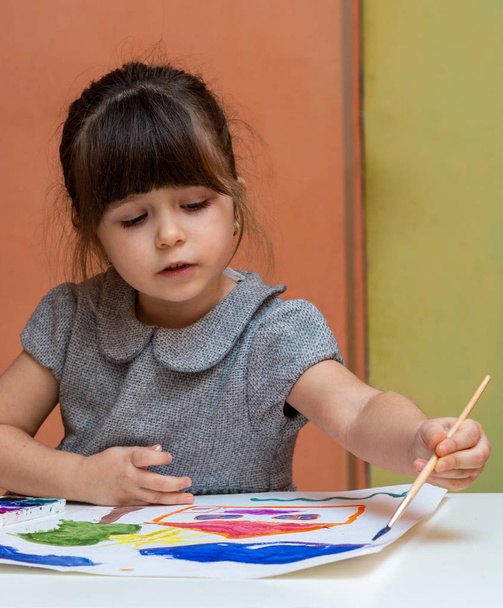 Маленька європейська дівчинка малює за столом у приміщенні. Дитина малює в своїй дитячій кімнаті вдома
 - Фото, зображення