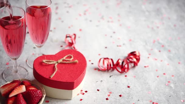 Láhev z růžové šampaňské, brýle s čerstvými jahodami a dárek ve tvaru srdce - Záběry, video