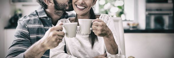 Man kissing on woman cheeks while having breakfast at home - Фото, зображення