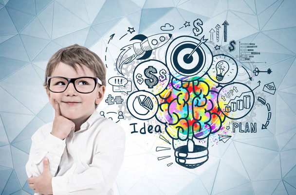 Adorable blond little boy wearing glasses and thinking standing near gray wall with geometric pattern and colorful business idea sketch. - Photo, image