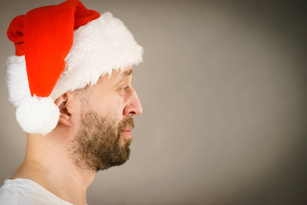 Bearded man wearing santa claus hat, side view on grey with copy space. Christmes time. - Фото, изображение