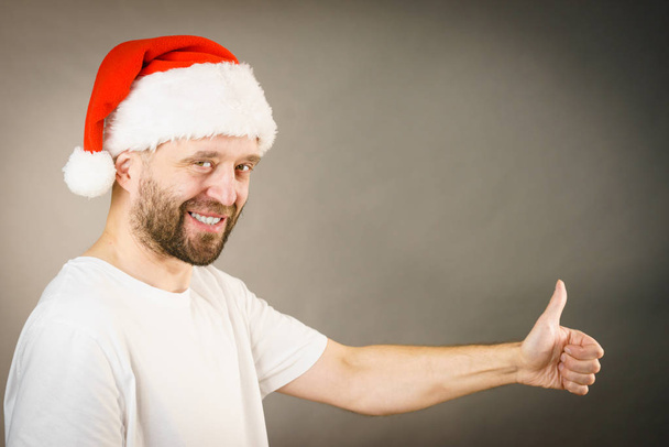 Bearded man wearing santa claus hat giving thumb up ok sign, on grey with copy space. Christmes time. - Photo, Image
