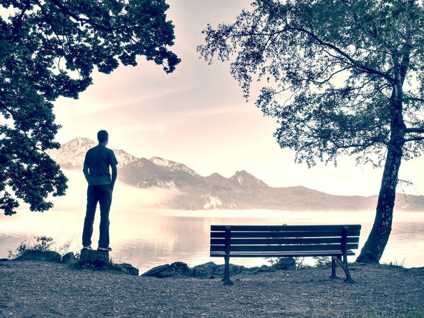 El hombre se queda solo en el banco frente al lago. Turista disfruta de hermosas vistas del lago de montaña
 - Foto, imagen