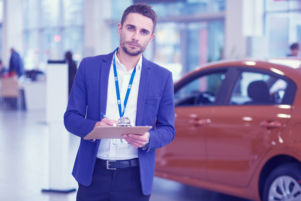 Dealer stands near a new car in the showroom - Photo, image