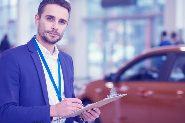 Dealer stands near a new car in the showroom - Foto, imagen
