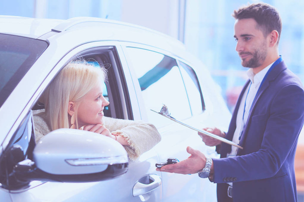 Car salesman sells a car to happy customer in car dealership and hands over the keys - Фото, изображение