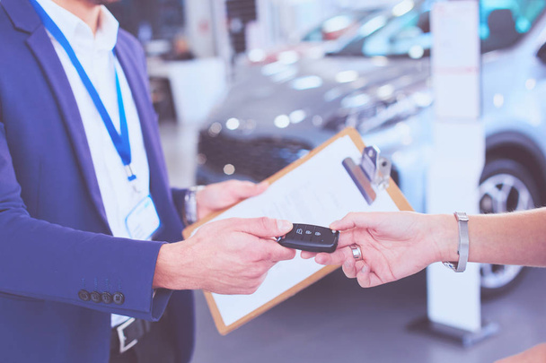 Car salesman sells a car to happy customer in car dealership and hands over the keys - Фото, зображення