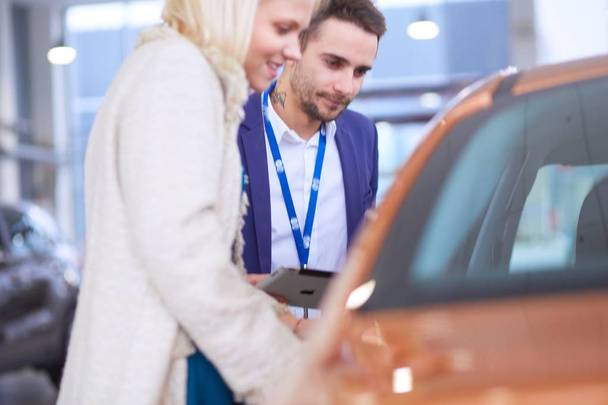 Dealer with woman stands near a new car in the showroom - Photo, Image