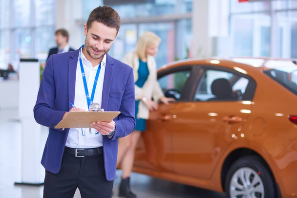 Dealer stands near a new car in the showroom - Foto, imagen