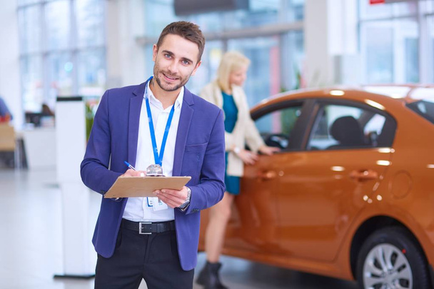 Dealer stands near a new car in the showroom - Photo, Image