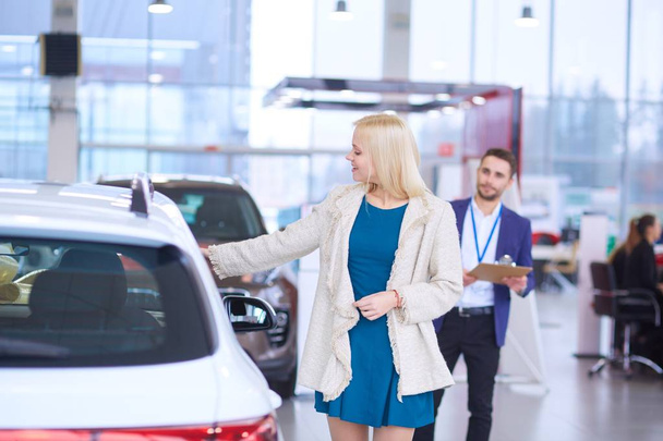 Dealer with woman stands near a new car in the showroom - Zdjęcie, obraz