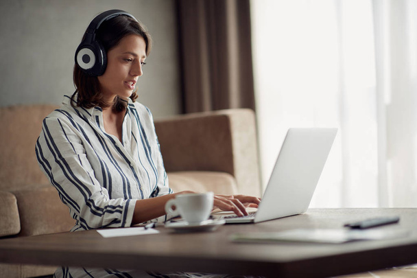 Young woman with headphones using laptop in her home - Фото, изображение