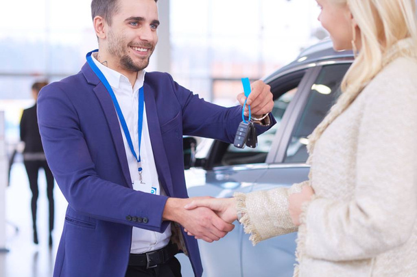 Image of car dealer handshaking with happy female in automobile center - Foto, immagini